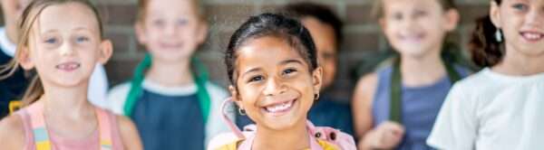 group of elementary students smiling at camera with hands around backpack straps